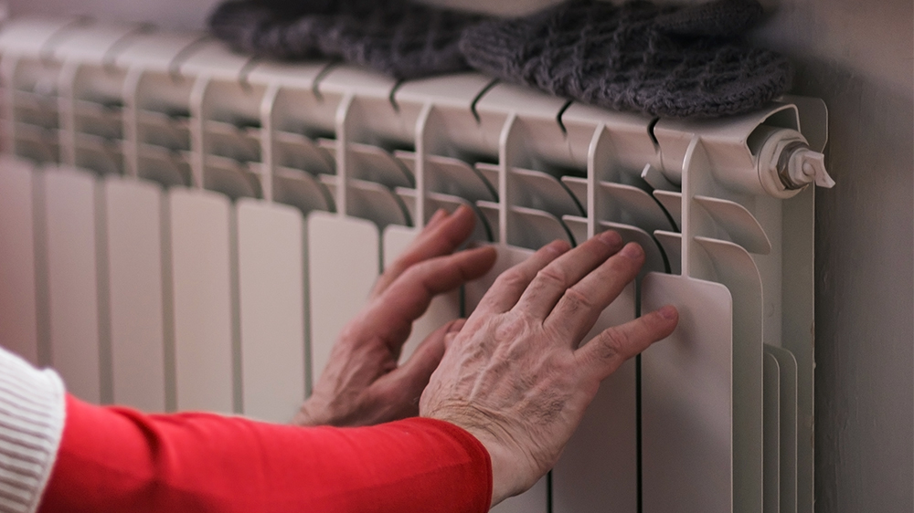 To hender som varmer seg på en radiator. På radiatoren ligger et par votter.
