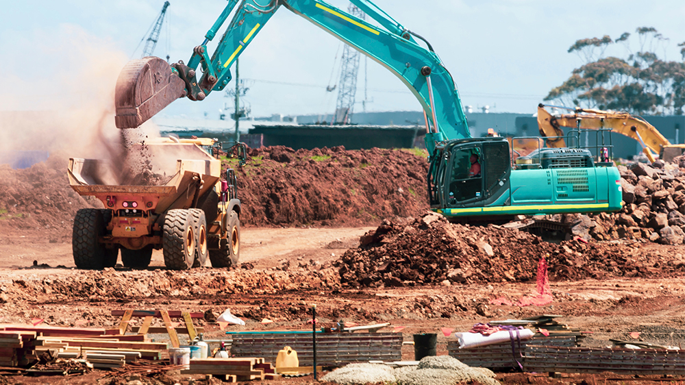 Gravemaskin fyller gravemasse på lastebil på en byggeplass